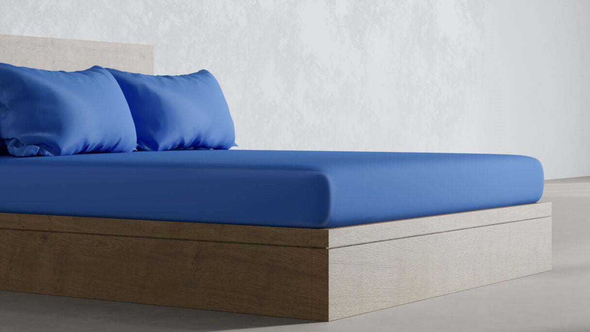 Modern bed with blue sheets and pillows in a minimalist bedroom setting.