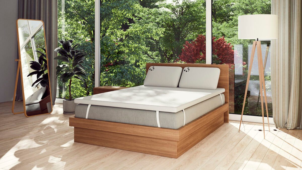 Modern bedroom with a wooden bed, mattress, and natural light from large windows.