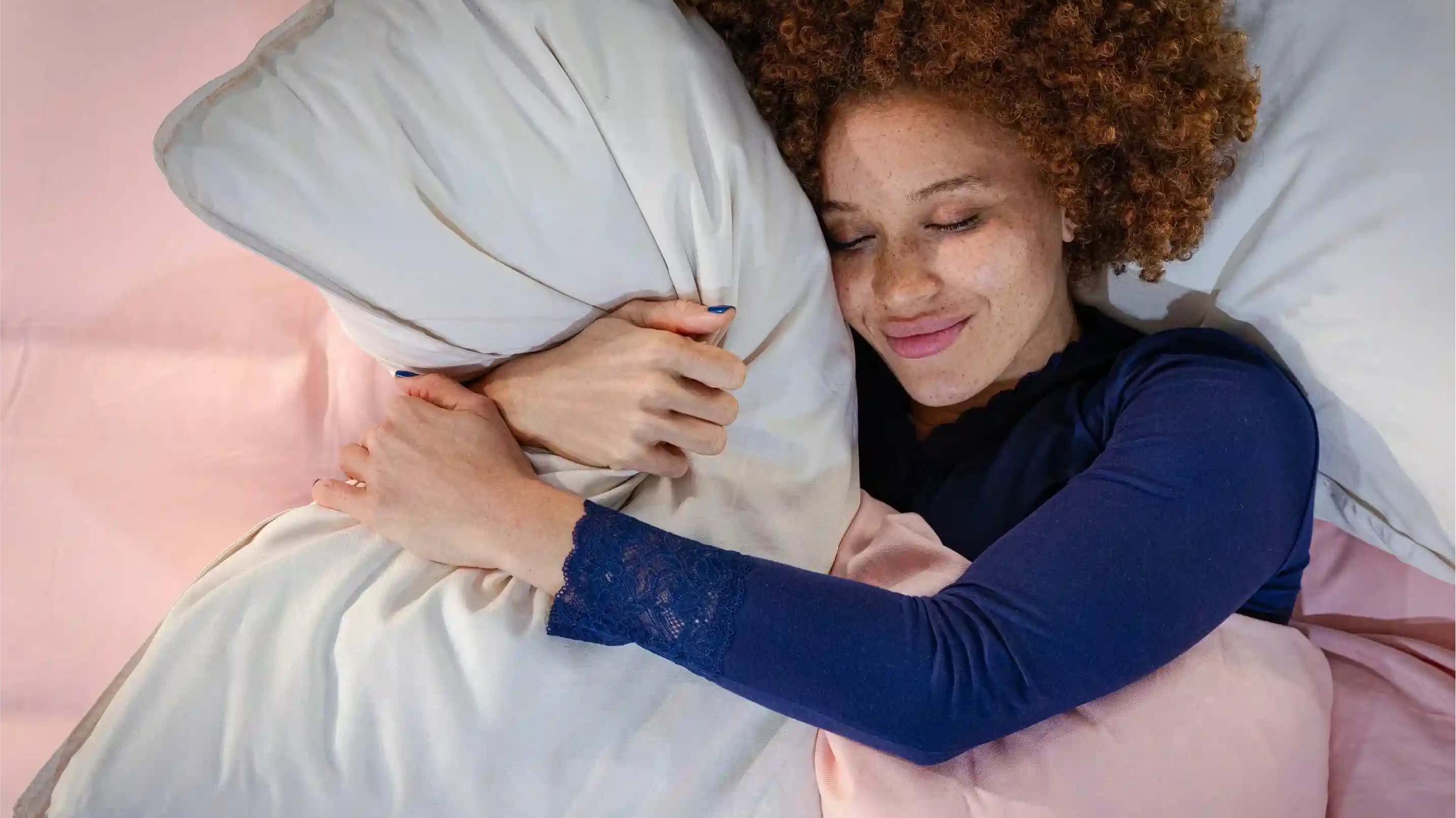Woman lying in bed hugging a pillow with pink bedding