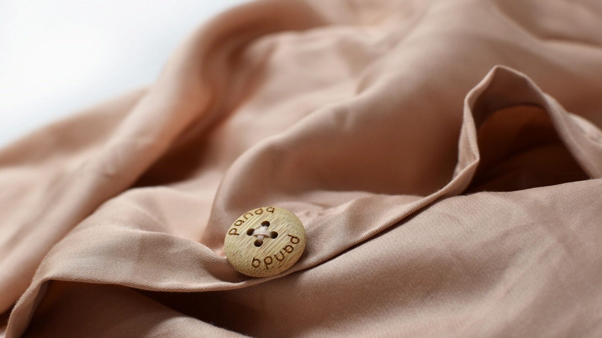 Close-up of a tan bedding fabric with a decorative wooden button on soft textiles.