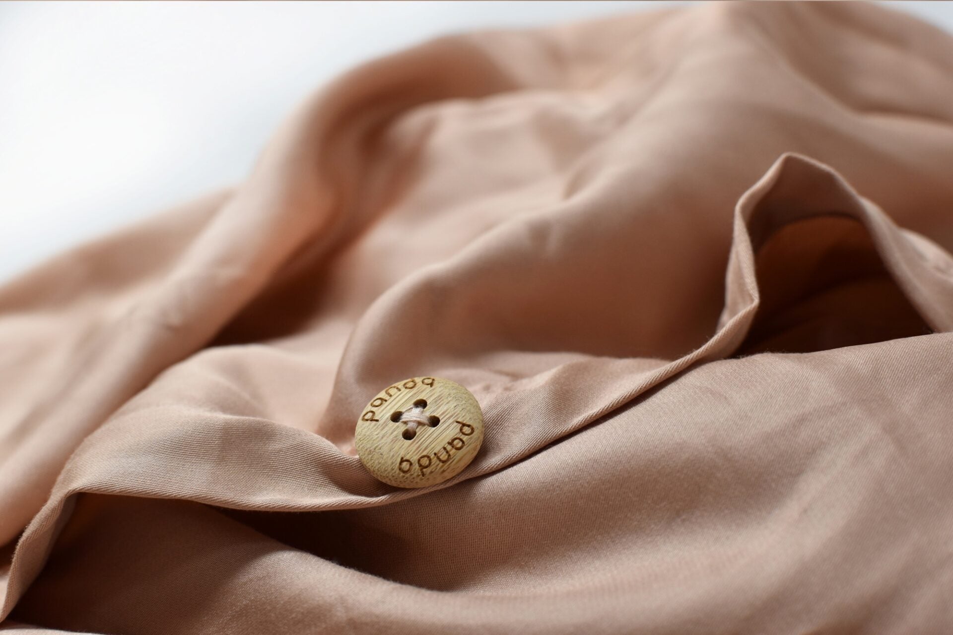 Close-up of a tan bedding fabric with a decorative wooden button on soft textiles.