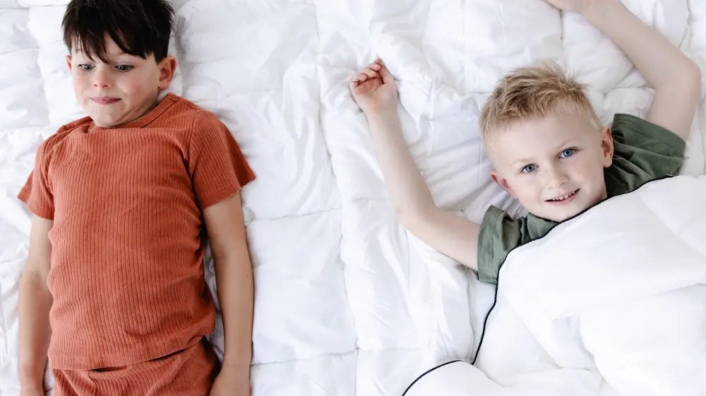Two children lying on a bed with a white duvet, showcasing comfort and warmth ideal for a duvet tog rating guide.