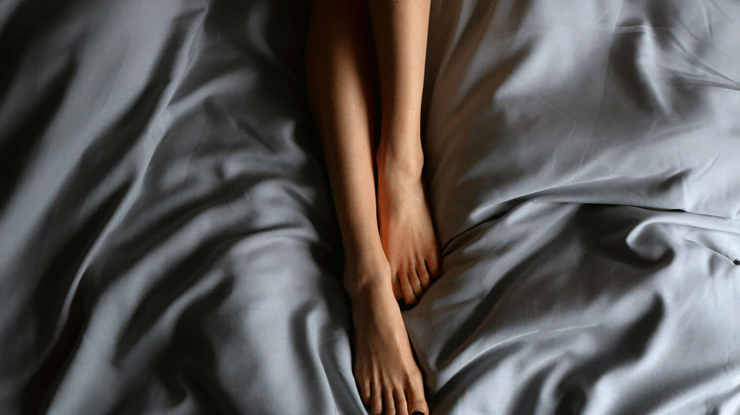 A pair of bare feet resting on smooth, wrinkled sheets, showcasing the comfort of bedding.