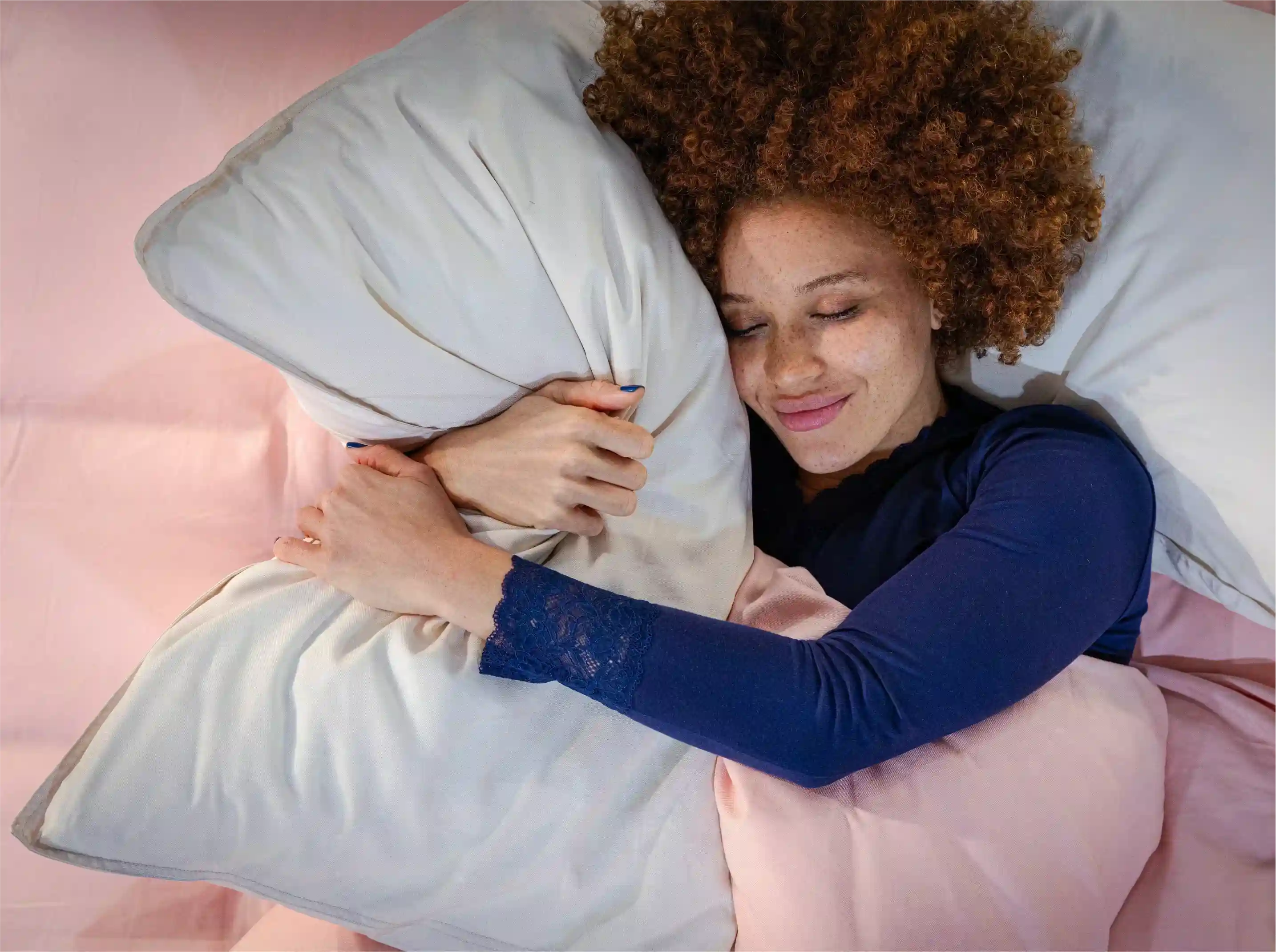 Woman lying in bed hugging a pillow with pink bedding