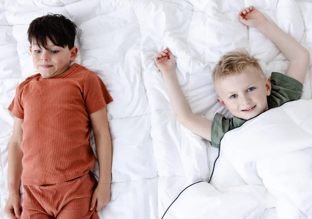 Two children lying on a bed with a white duvet, showcasing comfort and warmth ideal for a duvet tog rating guide.