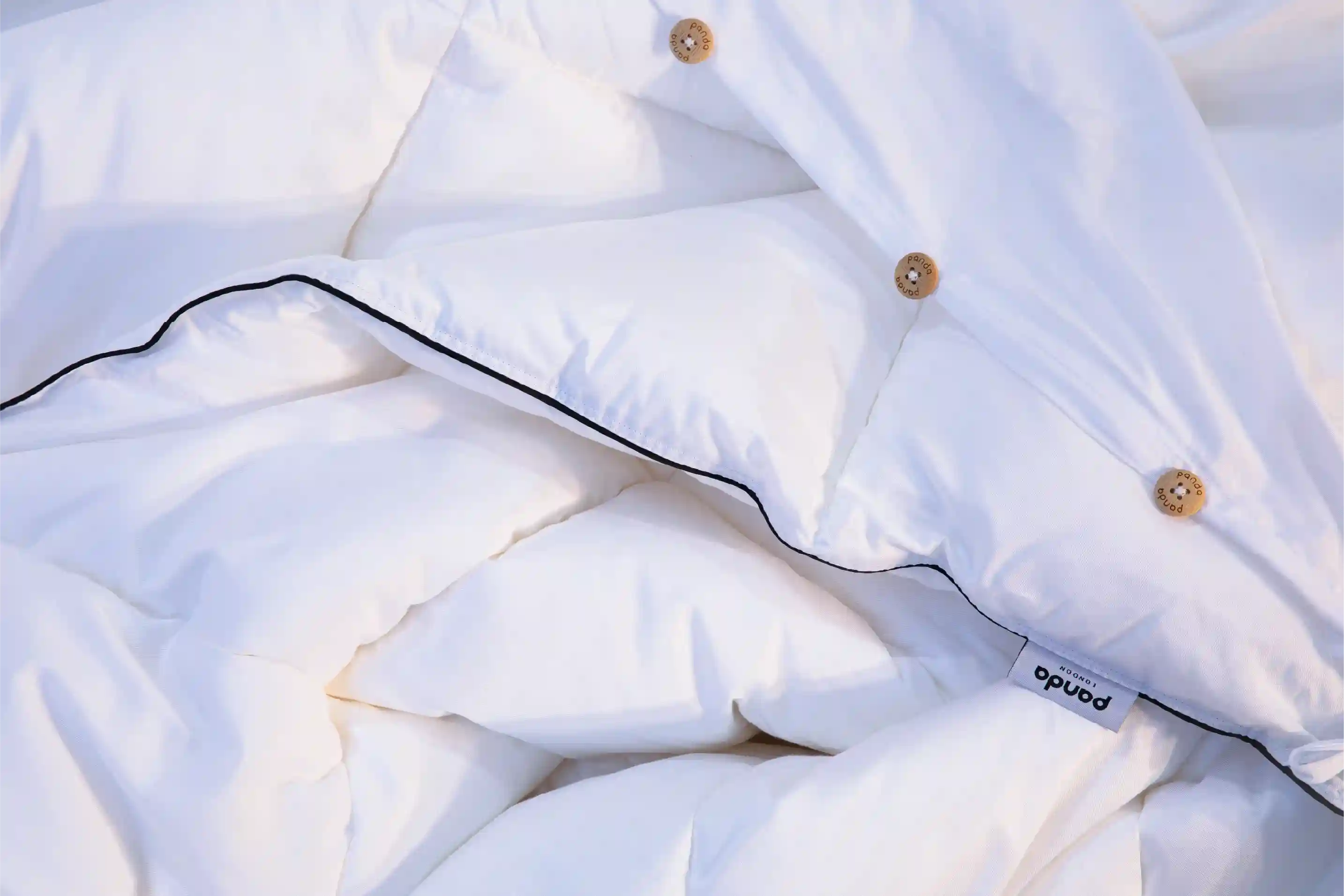 Close-up of a white cloud duvet with black piping, gold-tone buttons, and a small visible Panda label.