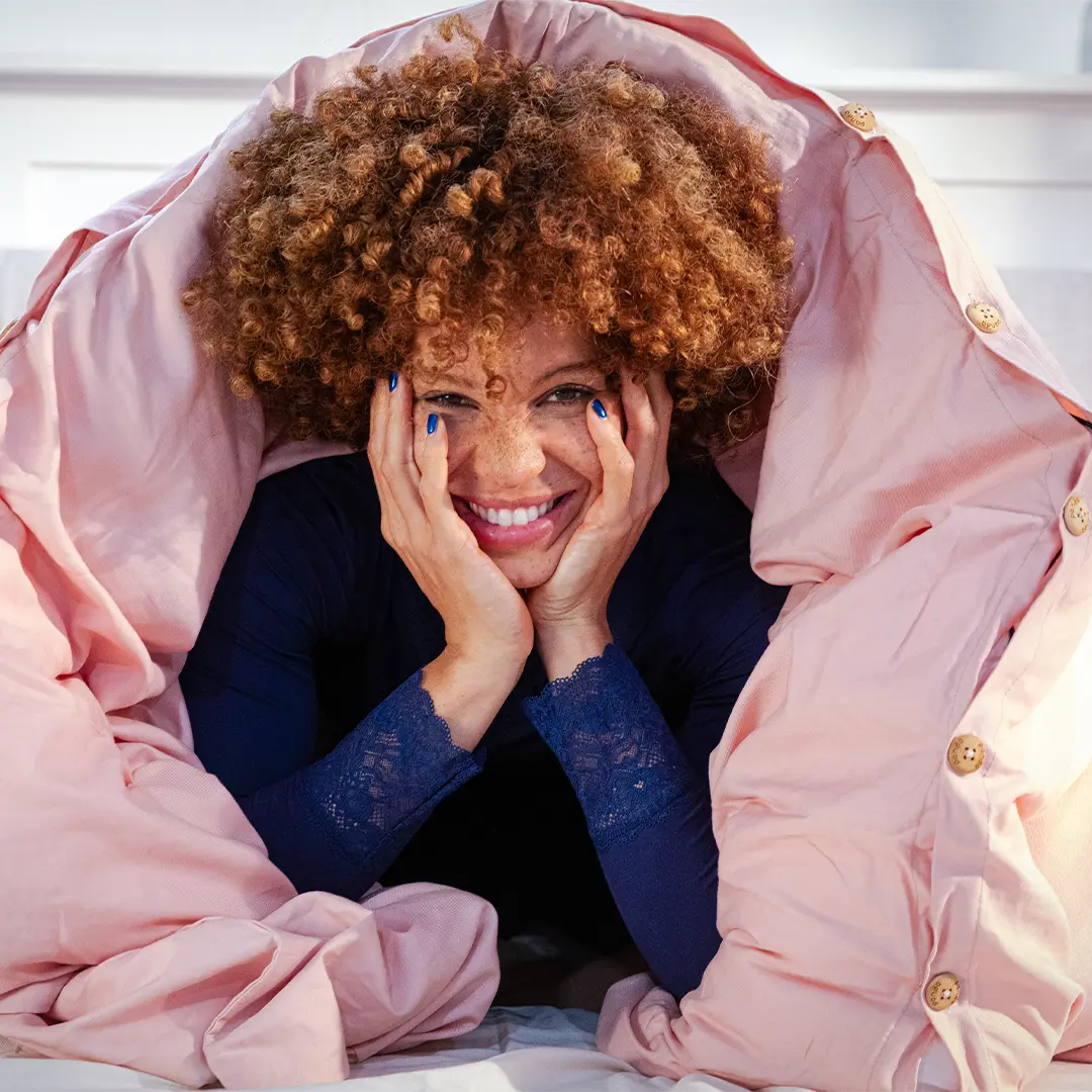 [HimalayanPink]  Woman smiling under bamboo and french linen duvet cover and looking 